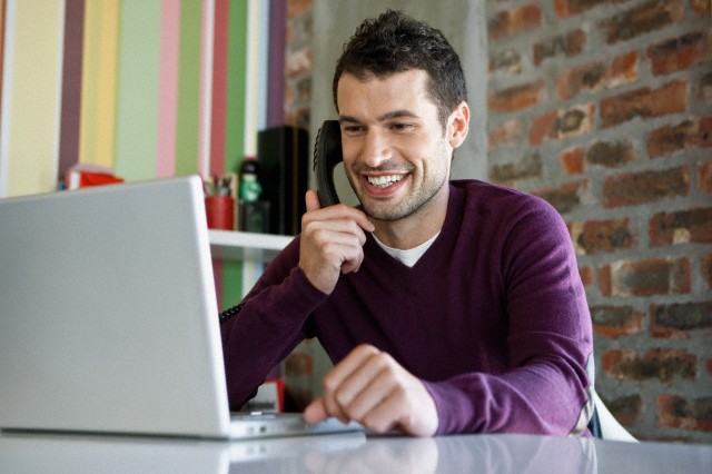 Imagen de diseñador de muebles de cocina hablando por teléfono frente a su laptop.